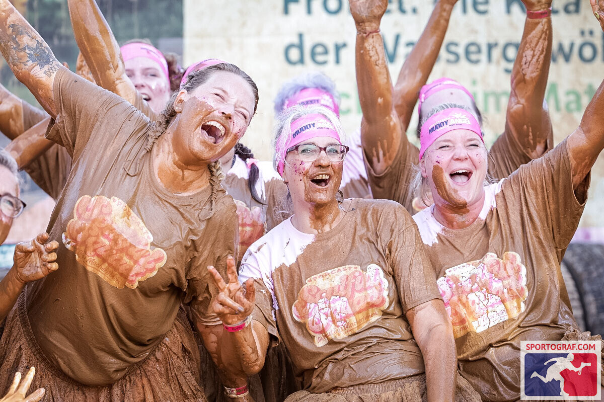 Drei Frauen aus dem Team lachen und jubeln voller Schlamm